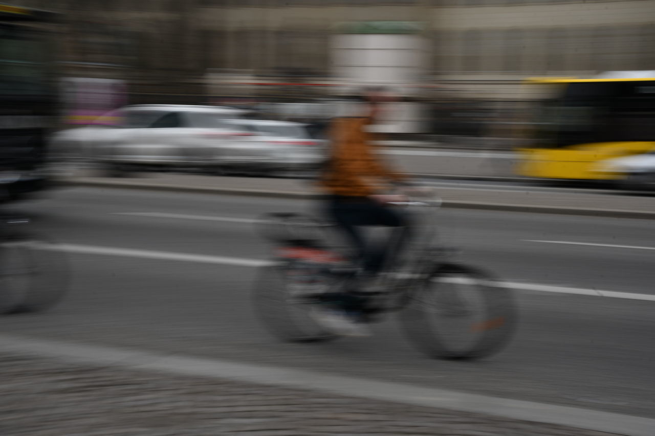 BLURRED MOTION OF MAN RIDING BICYCLE ON ROAD