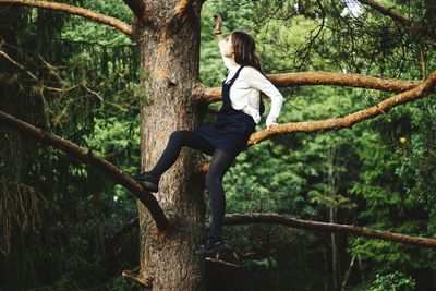 Full length of young woman sitting on tree trunk in forest