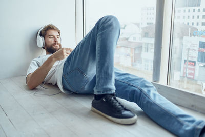 Young man looking down while sitting on window