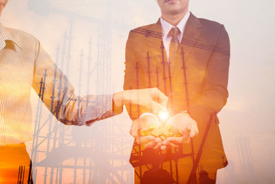 Double exposure of woman giving coins to businessman against oil drill during sunset