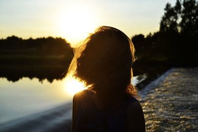 Girl standing at lakeshore against sky during sunset