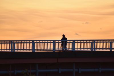 Silhouette man standing on footbridge against orange sky