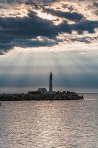 Lighthouse by sea and buildings against sky