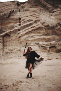 Full length of woman standing with baseball bat in desert against rock