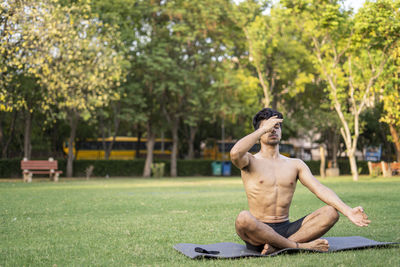 Full length of shirtless man sitting in park