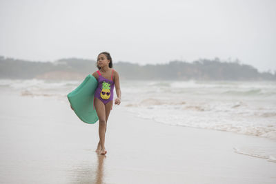 Girl holding swimming float walking at beach