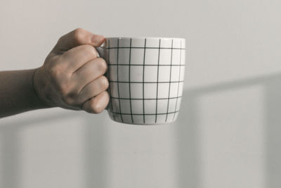Cropped hand of person holding coffee cup against white background