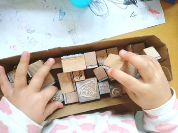 High angle view of baby hands holding wooden stamps in box on table