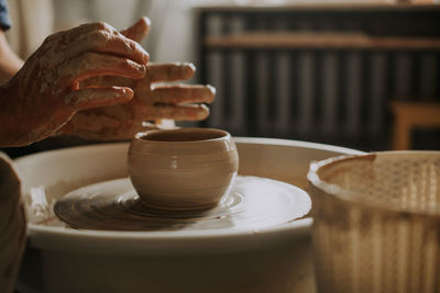 Close-up shot of ceramic cup spinning on potters's wheel and hands molding clay