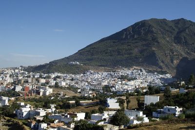 Aerial view of townscape by mountains against blue sky