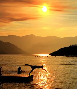 Scenic view of diving figure with sea against sky during sunset