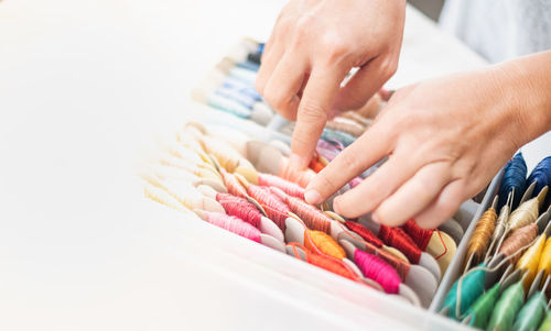 Close up hands of tailor woman choosing different colors thread in the box put on the table.