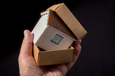 Close-up of hand holding model home in cardboard box against black background