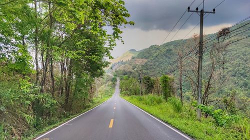 Road amidst trees and mountains against sky