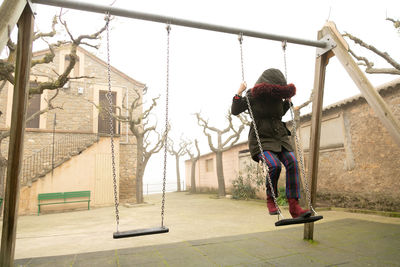 Young girl sheltered in an abandoned swing set with hood, unrecognisable.