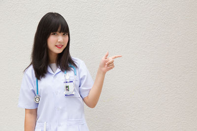 Young female doctor standing against wall