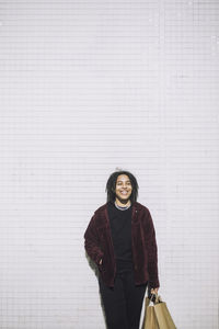 Happy non-binary person with shopping bags standing against wall