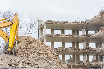 Low angle view of earth mover demolishing building against clear sky