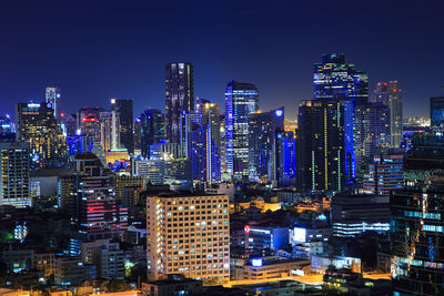 Illuminated modern buildings in city against sky at night