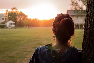 Rear view of woman standing by tree at park during sunset