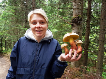 Portrait of smiling boy holding plant in forest