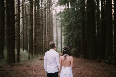 Rear view of man standing amidst trees in forest