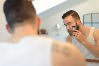 Young man shaving beard at home