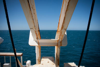 Scenic view of sea against clear blue sky through metallic structure