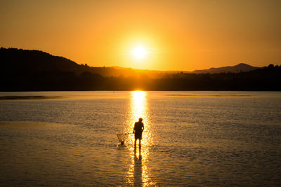 Silhouette people on sea against sky during sunset