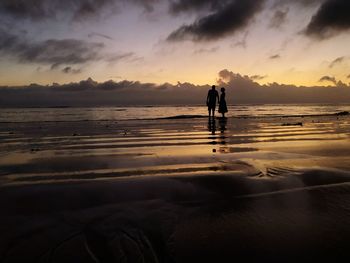 Silhouette couple standing in sea against sky during sunset