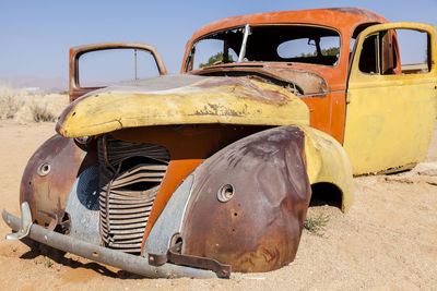 Abandoned car on sand against sky