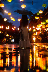 Rear view of woman standing against illuminated city at night