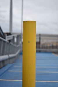 Close-up of yellow railing by bridge against sky