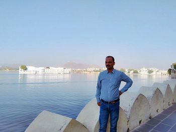 Portrait of man standing against blue sky and historical monument.