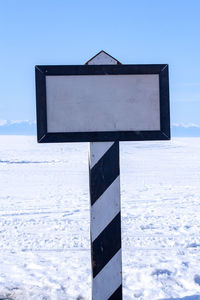 Road sign on snow covered field against sky