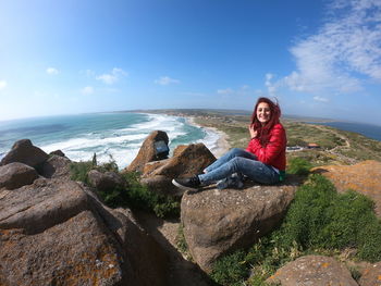 Young woman sitting on rock against sky
