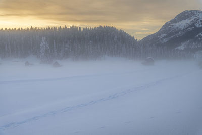 Snow covered land against sky during sunset