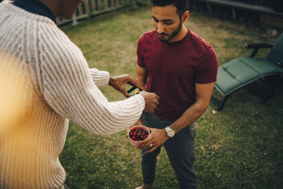 High angle view of man photographing cherries being held by friend in yard