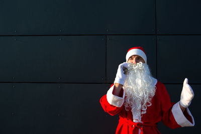 Man wearing costume taking on phone while standing against wall outdoors