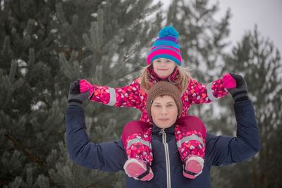 Portrait of brother carrying sister on shoulders against trees during winter