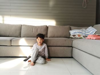 Boy holding remote control and sitting on floor against sofa at home