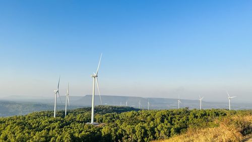 Windmills on field against clear blue sky