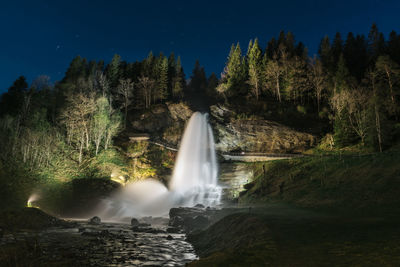 Waterfall in forest against sky at night