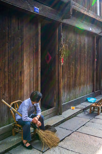 Full length of man sitting on wall in city