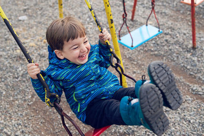 High angle view of cute boy playing on swing at playground