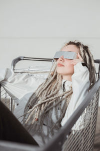 Young woman with dreadlocks sitting in shopping cart against wall