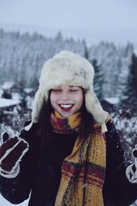 Cheerful young woman wearing warm clothing against trees during winter