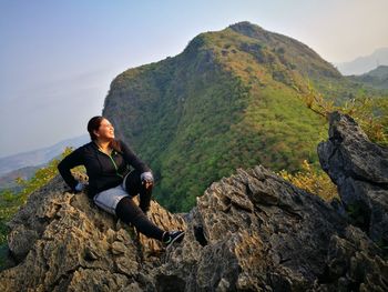 Man sitting on rock in mountains against clear sky