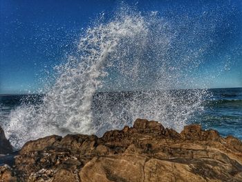 Water splashing on rocks from sea against blue sky
