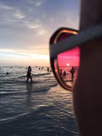 Reflection of man photographing on beach against sky during sunset